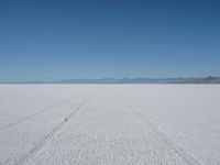 an empty landscape with a tire tracks in the middle and mountains behind it, near desert