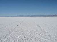 an empty landscape with a tire tracks in the middle and mountains behind it, near desert