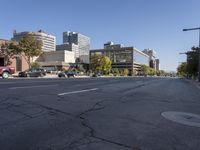 an empty street with cars on it near the city skyline and buildings on either side