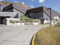 the entrance to a modern building surrounded by tall grass and shrubs, with blue skies