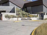 the entrance to a modern building surrounded by tall grass and shrubs, with blue skies