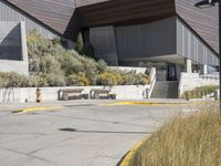 the entrance to a modern building surrounded by tall grass and shrubs, with blue skies