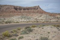 a man riding a motorcycle on a paved road in the desert next to rocks and shrubs