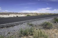 a black motorcycle is driving on the highway near the desert, against a blue sky with fluffy white clouds