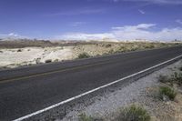 a black motorcycle is driving on the highway near the desert, against a blue sky with fluffy white clouds