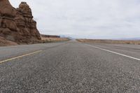 a lone motorcycle is traveling down the road past rocky formations in the desert, along with two yellow lines painted in white