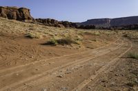 a desert road with some hills and rocks on one side and a blue sky above