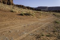 a desert road with some hills and rocks on one side and a blue sky above