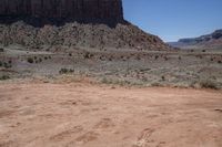 a person riding on a dirt bike near a mountain side valley with a red rock in the background