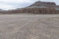 an empty field next to a big mountain with rocks in the background of the picture