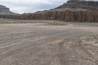 an empty field next to a big mountain with rocks in the background of the picture