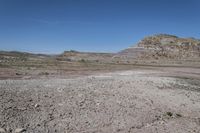 a vast rocky plain with some vegetation in the foreground and blue sky above it