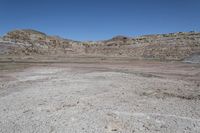 a vast rocky plain with some vegetation in the foreground and blue sky above it