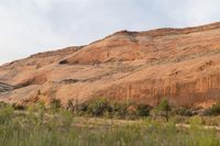 red rocks on the cliff side in an area with bushes and trees, with the sky overhead