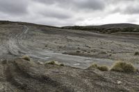 dirt track going across the middle of a desert field with cloudy skies in the background