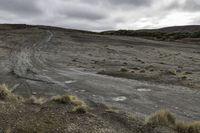 dirt track going across the middle of a desert field with cloudy skies in the background