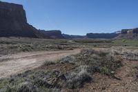 the dirt road is in a barren valley with mountains in the background, with a blue sky overhead