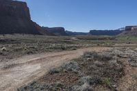 the dirt road is in a barren valley with mountains in the background, with a blue sky overhead