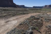 the dirt road is in a barren valley with mountains in the background, with a blue sky overhead