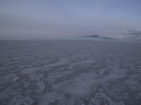 an ocean covered in a thick layer of snow with low clouds coming up around the mountains