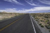 the empty road is lined with gravel and plants while the sky looks blue in the background