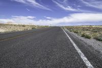 the empty road is lined with gravel and plants while the sky looks blue in the background