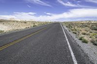 the empty road is lined with gravel and plants while the sky looks blue in the background