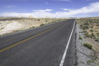 the empty road is lined with gravel and plants while the sky looks blue in the background