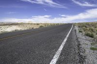 the empty road is lined with gravel and plants while the sky looks blue in the background