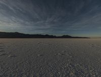 a wide open plain with a mountain in the background and some clouds above it in the distance