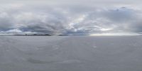 some clouds are above the snow field and mountains as seen from the ground on a camera