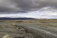 an empty road surrounded by barren mountains and bushes under a cloudy sky, as if in nature