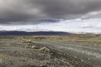 an empty road surrounded by barren mountains and bushes under a cloudy sky, as if in nature