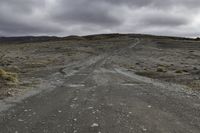 an empty dirt road that is running across a vast plain, with a few vehicles on the sides