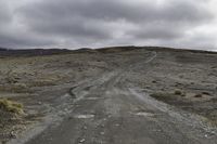 an empty dirt road that is running across a vast plain, with a few vehicles on the sides