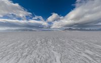 wide snowy plain under blue skies with mountains in background and clouds in the sky above