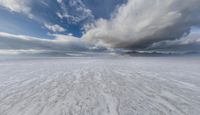 wide snowy plain under blue skies with mountains in background and clouds in the sky above