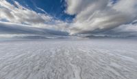 wide snowy plain under blue skies with mountains in background and clouds in the sky above