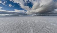 wide snowy plain under blue skies with mountains in background and clouds in the sky above