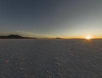 a man walking across an open field in the sun setting down on the horizon towards mountains