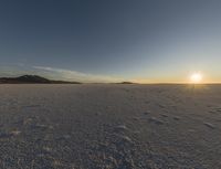 a man walking across an open field in the sun setting down on the horizon towards mountains