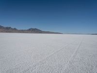 a wide expanse with footprints running across the snow in the foreground and mountains in the distance