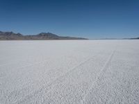 a wide expanse with footprints running across the snow in the foreground and mountains in the distance