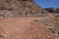 a dirt road through a desert plain with a mountain behind it and a clear blue sky in the background