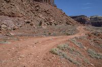 a dirt road through a desert plain with a mountain behind it and a clear blue sky in the background