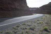 a person riding a motorcycle along a narrow road through rocks and sand cliffs a grassy area on both sides