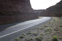 a person riding a motorcycle along a narrow road through rocks and sand cliffs a grassy area on both sides