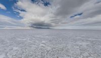 an image of the ice on the beach in front of some mountain peaks and a cloudy sky