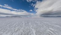 an image of the ice on the beach in front of some mountain peaks and a cloudy sky