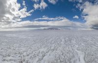 an image of the ice on the beach in front of some mountain peaks and a cloudy sky